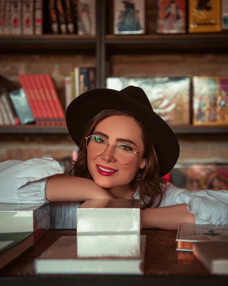 a woman wearing glasses and a hat leaning on a table